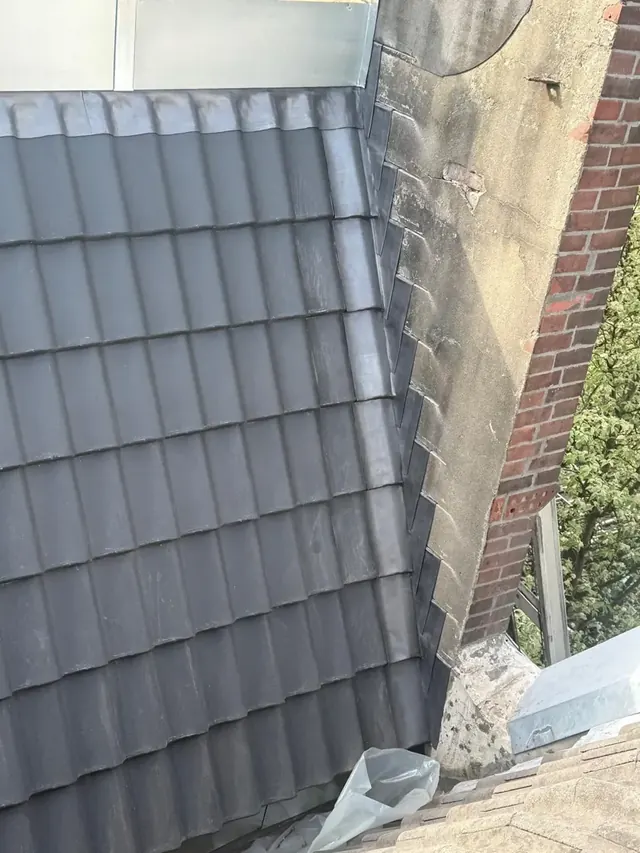 Pannen langs een schoorsteen — De aansluiting van nieuwe dakpannen op het metselwerk van een schoorsteen.